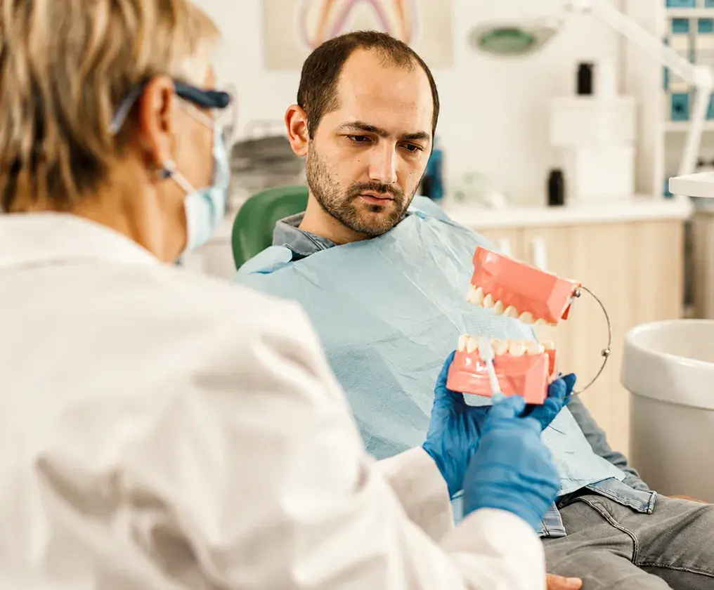 A smiling clinician demonstrating brushing on a dental model for a seated patient