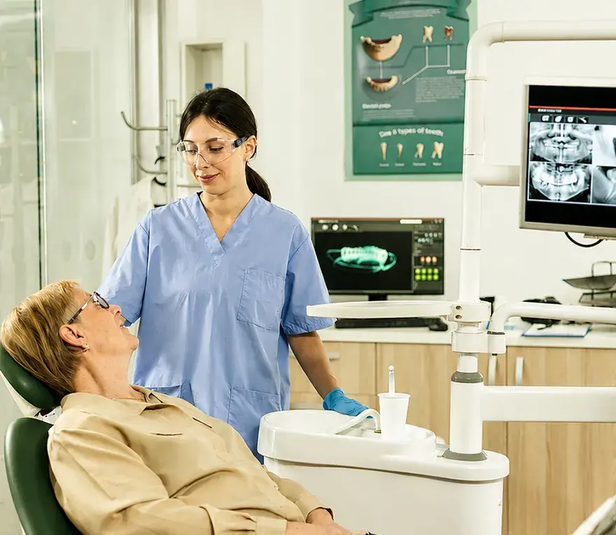 A dental assistant reviewing scans with a smiling patient in the treatment chair