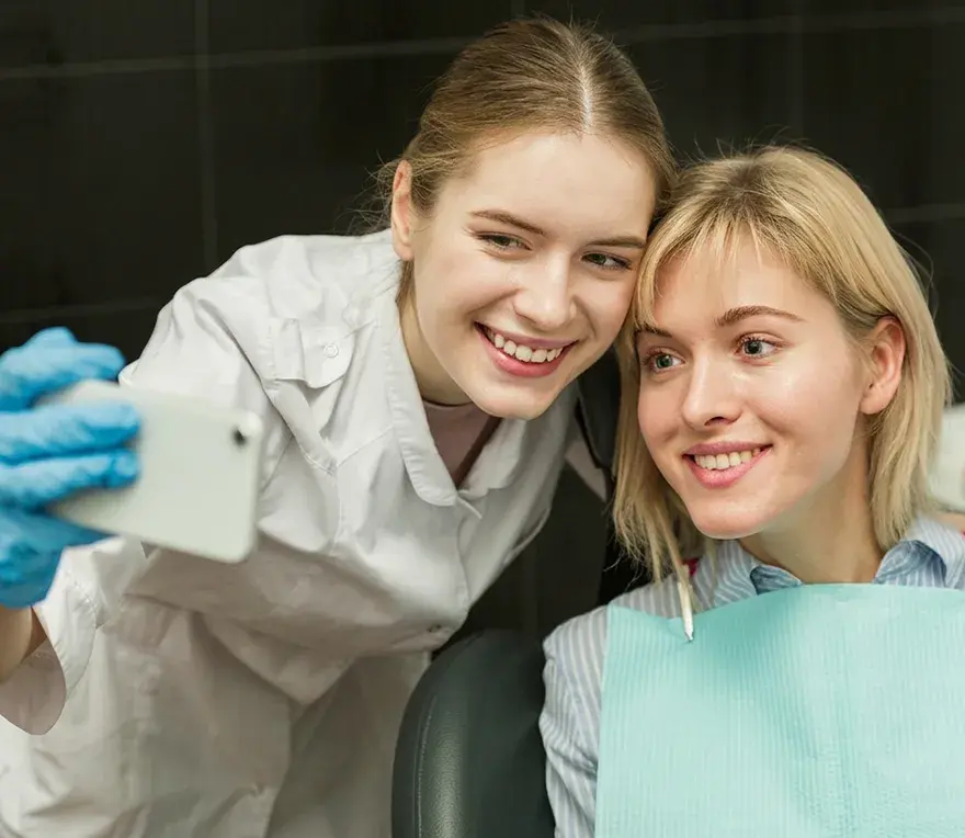 A dental assistant and a smiling patient taking a selfie together in the treatment chair